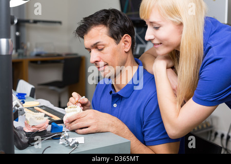 Woman watching dental technician applying porcelain to mold with a brush Stock Photo