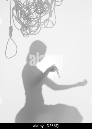 side view of woman holding a syringe with needle on top of her arm, with tangled hanging rope on top of her head, behind a diffu Stock Photo