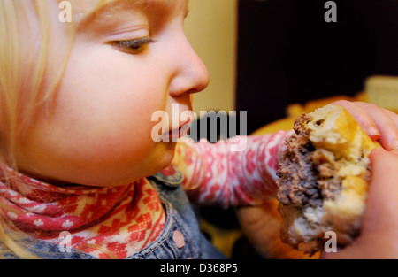 A young girl eats a hamburger with chips and tomato sauce at the table for her dinner Stock Photo