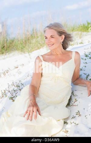 Happy senior woman looking out to sea on a deserted tropical beach with bright clear blue sky laying in the sand Stock Photo