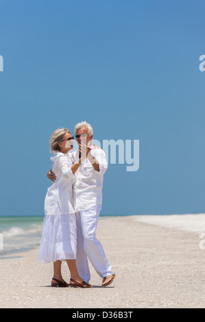 Happy senior man and woman couple together dancing by the sea on a deserted tropical beach with bright clear blue sky Stock Photo
