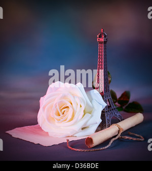Picture of beautiful retro style still life over blue grunge background, white fresh rose flower, small decorative Eiffel tower Stock Photo