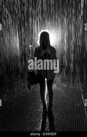 Silhouette of woman wearing hooded coat standing on a grilled metal floor in the rain with light coming from behind. Stock Photo