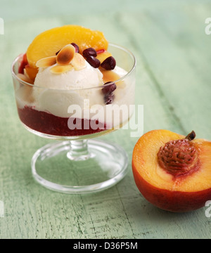 Peach Melba: vanilla ice cream with fresh peach slices and raspberry sauce garnished with pomegranate seeds and almond slices. Stock Photo