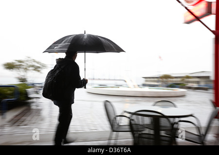 man with backpack and umbrella walking hurrying in the rain north Vancouver BC Canada deliberate motion blur Stock Photo