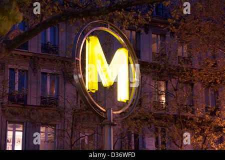 The bright yellow “M” symbol, is a modern version of the Paris Metro sign, marking the entrance to the Bastille station. Illuminated at night. France. Stock Photo