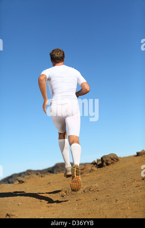 Back view of male athlete wearing compression clothes, shorts, socks running in countryside against clear blue sky Stock Photo
