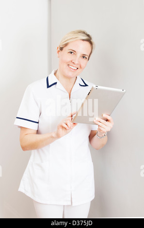 Smiling female wearing a white medical uniform holding a digital tablet. Stock Photo