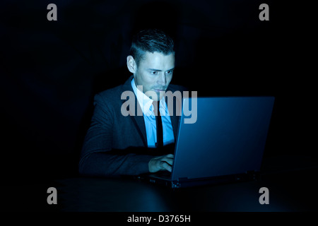 a smiling man working on a laptop computer during the night or in a darkened room Stock Photo