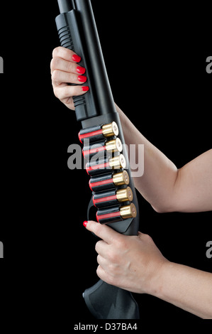 A woman with red fingernails holds onto a 12 gage shotgun with clips of ammunition. Stock Photo