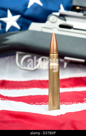 A single bullet in front of an assault rifle sitting on an American flag. Stock Photo