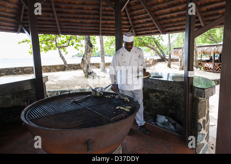 Hotel chef cooks fish on a large barbeque alongside the beach in St Lucia, West Indies. Stock Photo