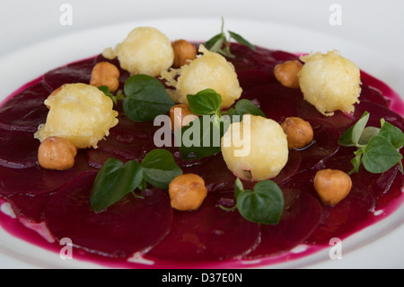 Beetroot carpaccio with candid hazelnut, and goats cheese tempura served on a white plate Stock Photo