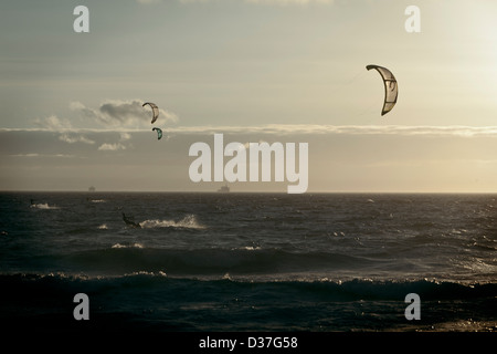 Two Kite surfers enjoy the last surf of the day as a cargo ship passes in the background on Blouberg Beach. Stock Photo