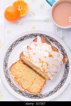 Citrus lemon orange clementine drizzle iced sponge cake homemade on a floral tablecloth with a Clementine and a cup of tea. Stock Photo