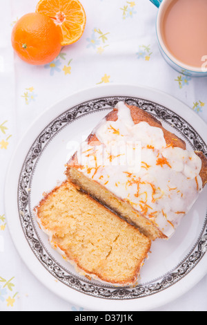 Citrus lemon orange clementine drizzle iced sponge cake homemade on a floral tablecloth with a Clementine and a cup of tea. Stock Photo