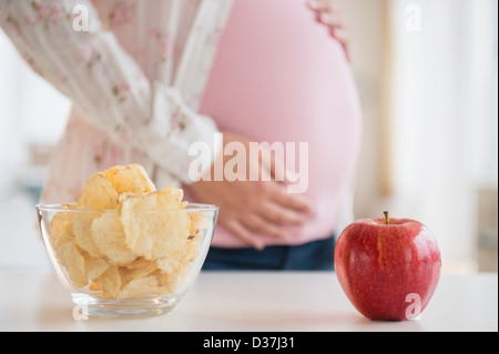 Pregnant woman choosing between apple and chips Stock Photo