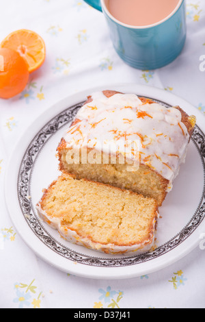 Citrus lemon orange clementine drizzle iced sponge cake homemade on a floral tablecloth with a Clementine and a cup of tea. Stock Photo