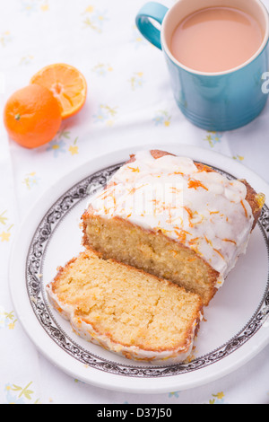 Citrus lemon orange clementine drizzle iced sponge cake homemade on a floral tablecloth with a Clementine and a cup of tea. Stock Photo