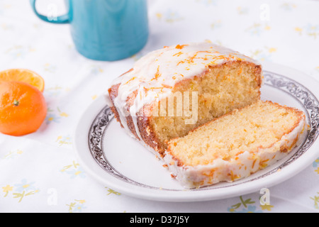 Citrus lemon orange clementine drizzle iced sponge cake homemade on a floral tablecloth with a Clementine and a cup of tea. Stock Photo