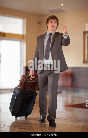 Businessman rolling luggage in lobby Stock Photo