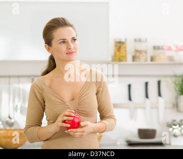 Portrait of thoughtful young woman with apple in modern kitchen Stock Photo