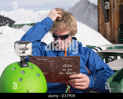 Man thinking scratching his head whilst trying to decide what to eat from a menu outside Gite du Lac de Gers ski restaurant in winter. Samoens France Stock Photo