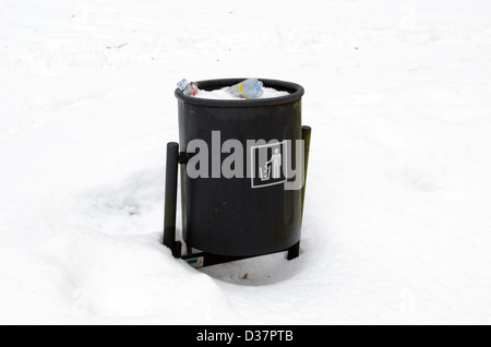 full garbage dustbin waste bin surrounded by snow in winter park. Stock Photo