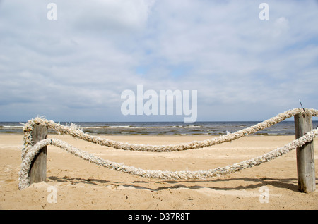 fence made of logs and thick rope on seaside beach sand and sea ocean in background. Stock Photo