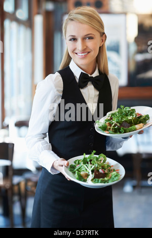 Denmark, Aarhus, Portrait of young waitress holding plates with salad Stock Photo