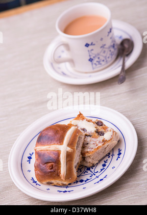 Toasted hot cross bun buttered with a cup of tea served on patterned vintage china crockery on a neutral table cloth. Stock Photo