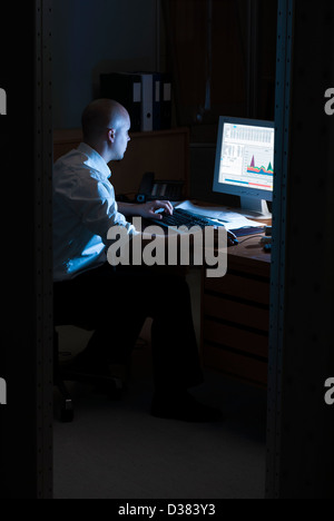 Late night office worker working overtime. White collar worker working on computer at night in dark office. Stock Photo