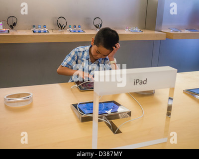 A 7-9 year old Asian boy is engrossed in a computer game on an iPad in an Apple Store. Stock Photo