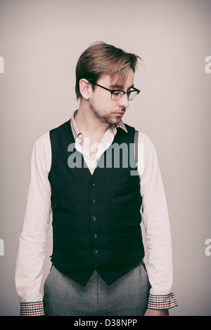 Man in twenties in black waistcoat, white shirt, grey trousers and glasses looks thoughtful. Stock Photo