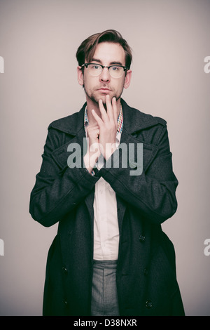 Man in twenties in grey coat, white shirt, grey trousers and glasses looks surprised. Stock Photo