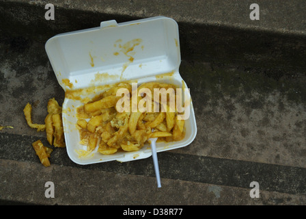 Fish and Chips and takeaway carton discarded on pavement with plastic fork. Stock Photo