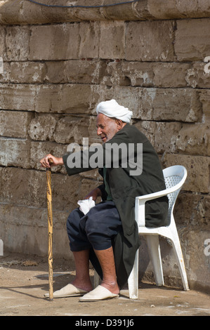 Old Moroccan man with a walking stick sitting infront of the walls surrounding Essaouira Harbour, Essaouira, Morocco Stock Photo