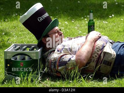(dpa) - A man wearing a huge 'Guinness' hat is dozing on the lawn at the end of a drinking spree on Father's Day in Leipzig, Germany, 9 May 2002, an unfinished bottle of beer resting on his belly. As a tradition, fathers are celebrating their day with heavy drinking, while devoted Christians are hol Stock Photo