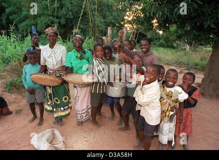 (dpa) - Children gather around women grinding corn in the village of Kalambo, northern Malawi, 13 June 2001. Unicef supports child care projects in the village that has a high percentage of AIDS infected people, among them babies who acquired the infection in the womb. Many children have lost their  Stock Photo