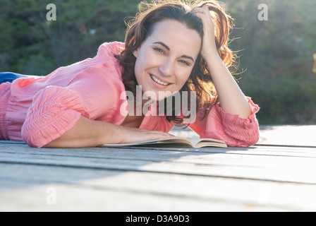 Smiling woman reading on deck Stock Photo