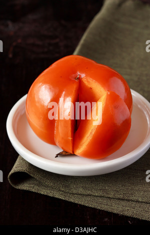 Ripe persimmon fruit in a plate on a brown wooden background. Stock Photo