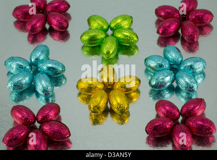 Brightly coloured foil wrapped Easter Eggs arranged in star shapes on a reflective silver background. Stock Photo