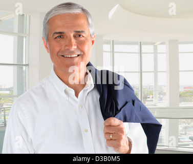 Portrait of a casually dressed businessman in a modern office building. Man is smiling holding his jacket over his shoulder. Stock Photo