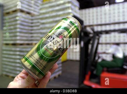 (dpa) - A hand holds a can of beer in the foreground and a pallet carrier arranges in the background pallets of beer in the warehouse of the Holsten Brewery in Hamburg, 23 January 2003. The brewery announced on 22 January that around 600 members of staff are to work reduced hours due to the decrease Stock Photo