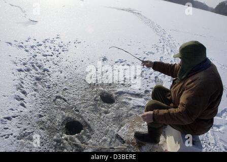 (dpa) - A man dressed in warm winterclothes is holding a fishing rod into a hole in the ice covering the Wannsee lake in Berlin, 7 January 2003. Stock Photo
