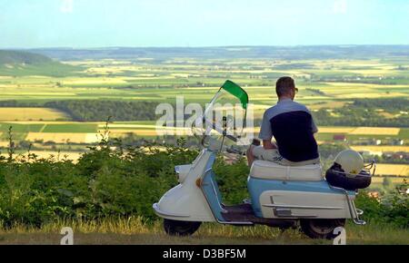 (dpa) - A jung man sits on his 43-year-old scooter of the type Heinkel and enjoys the panormaic view of the landscape at Iphofen, Germany, 26 June 2003. Stock Photo