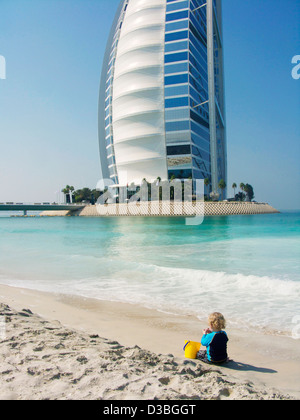 The seven star 'Sail in the Desert' Burj al Arab luxury hotel in the background of a small boy playing on the beach in Dubai UAE Stock Photo