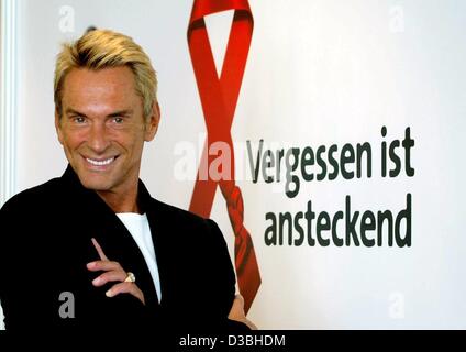 (dpa) - German fashion designer Wolfgang Joop stands with folded arms in front of a poster which reads 'to forget is contagious' and smiles after a press conference in Hamburg, Germany, 16 May 2003. The 58-year-old designer will be awarded the 'Red Award' in the context of a charity gala for the Ger Stock Photo
