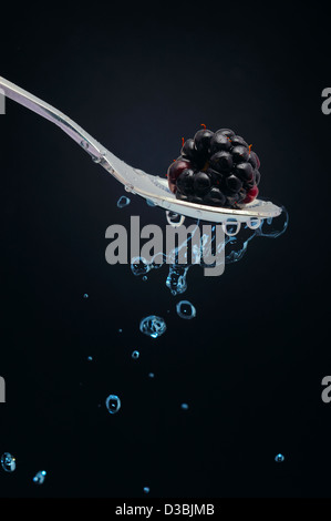 Teaspoon with blackberry and dripping natural mineral water in black background. Stock Photo