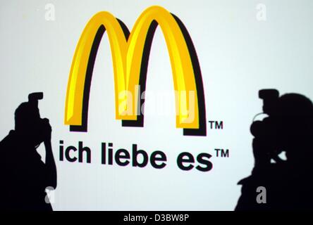 (dpa) - Two journalists take a photo of the new logo of the fast food chain McDonald's during a press conference in Munich, 2 September 2003. The slogan 'ich liebe es' ('i'm lovin' it') will soon make its way into the vocabulary of McDonald's customers in more than 100 countries as the Golden Arches Stock Photo